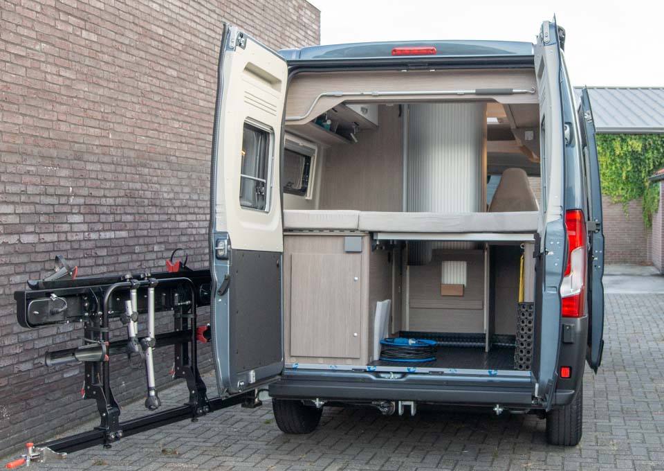 Achterzijde van huurcamper P&ouml;ssl 2Win R S met geopende achterdeuren en een zee van opbergruimte onder het bed